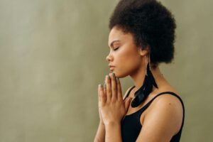 The individual’s hands are pressed together in front of their chest (Anjali Mudra), which is a traditional yoga gesture symbolizing centeredness, gratitude, and mindfulness.